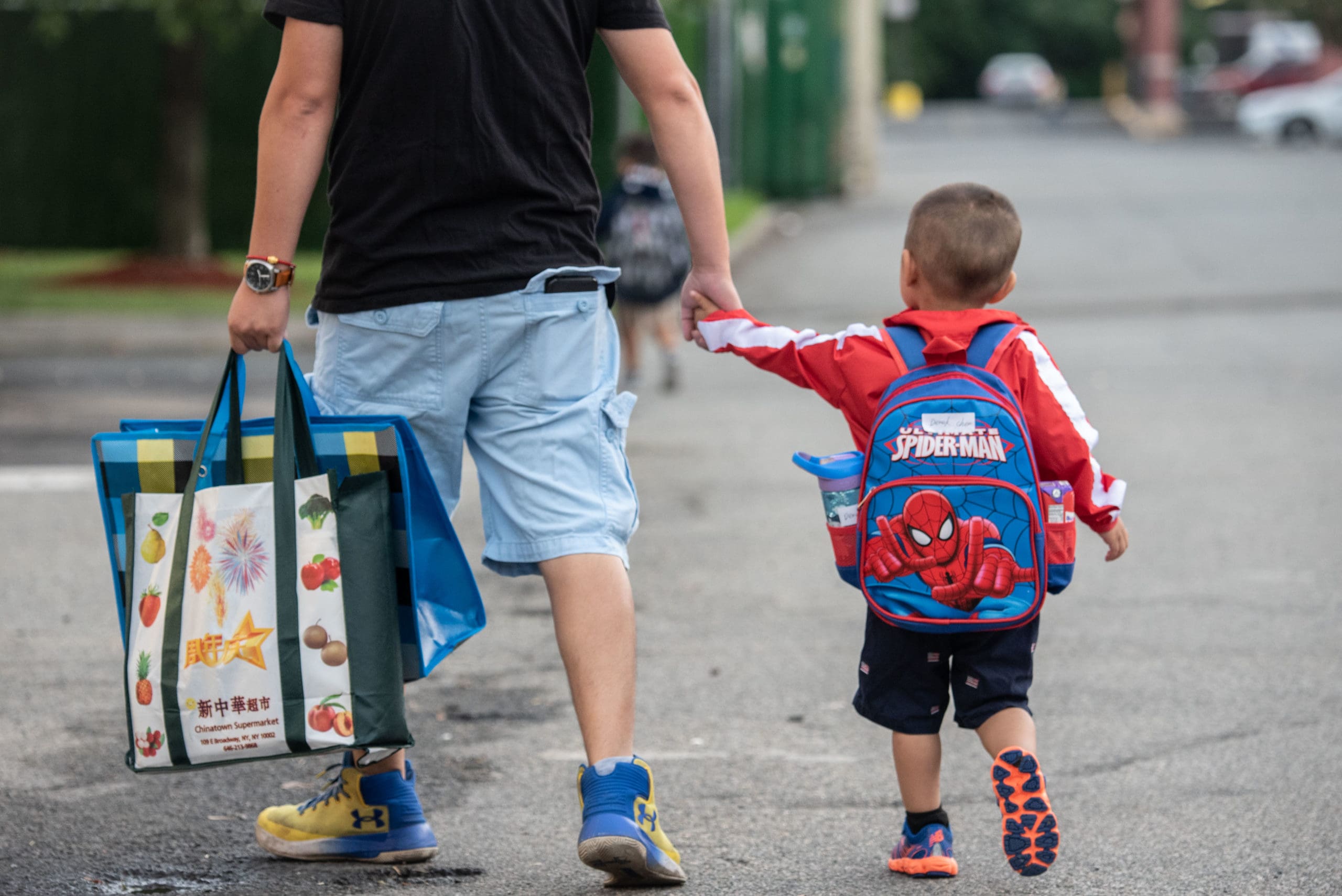 A father holds hands and walks with his child wearing a backpack